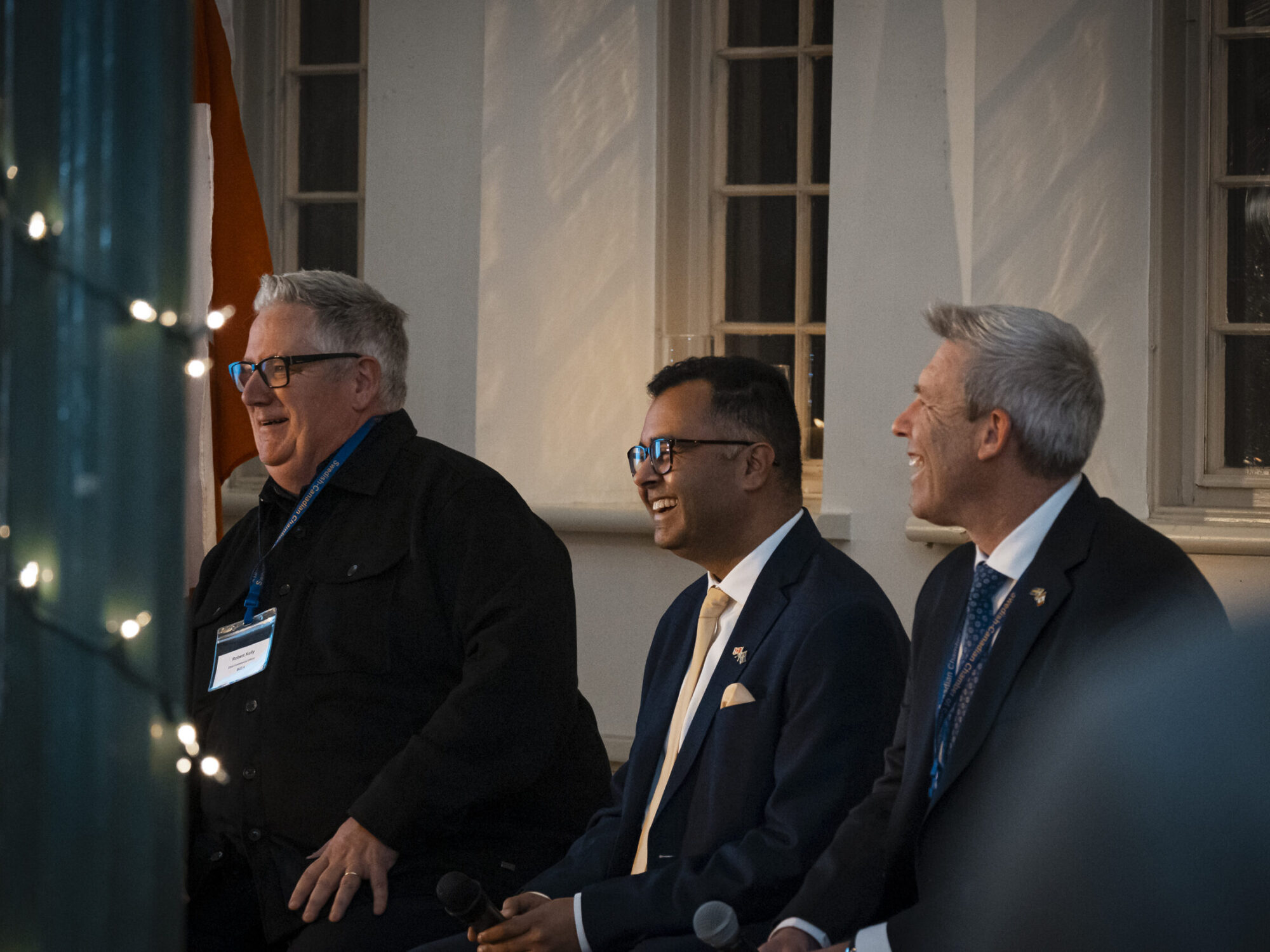 Photo of three men smiling while participating as panelists at an event. Photo of three men smiling while participating as panellists at an event.