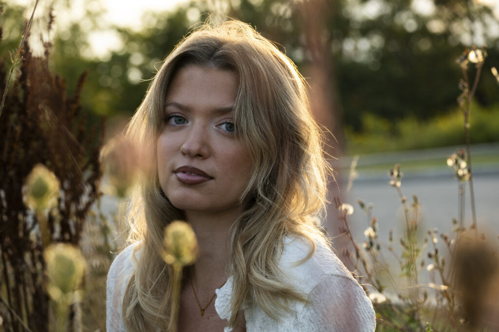 A portrait of a young woman outdoors, surrounded by soft-focus plants.